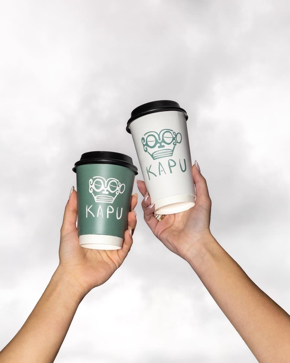 Two KAPU cups held up against an open sky